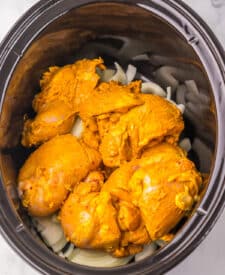 Juicy chicken shawarma thighs in the slow cooker surrounded by onions