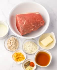 Raw eye of round roast with seasoning ingredients including garlic, gravy mix, ranch mix, and broth.