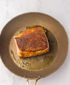 Seasoned eye of round roast searing in a skillet.