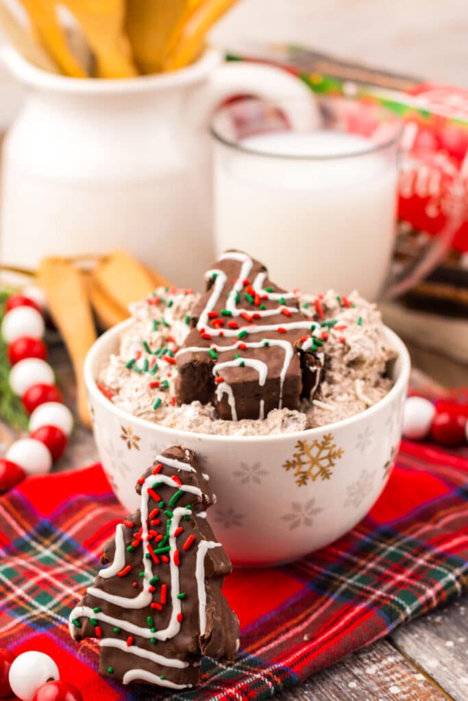 Chocolate Christmas Tree Cake Dip topped with red and green sprinkles and mini Christmas tree cakes on a festive red plaid tablecloth