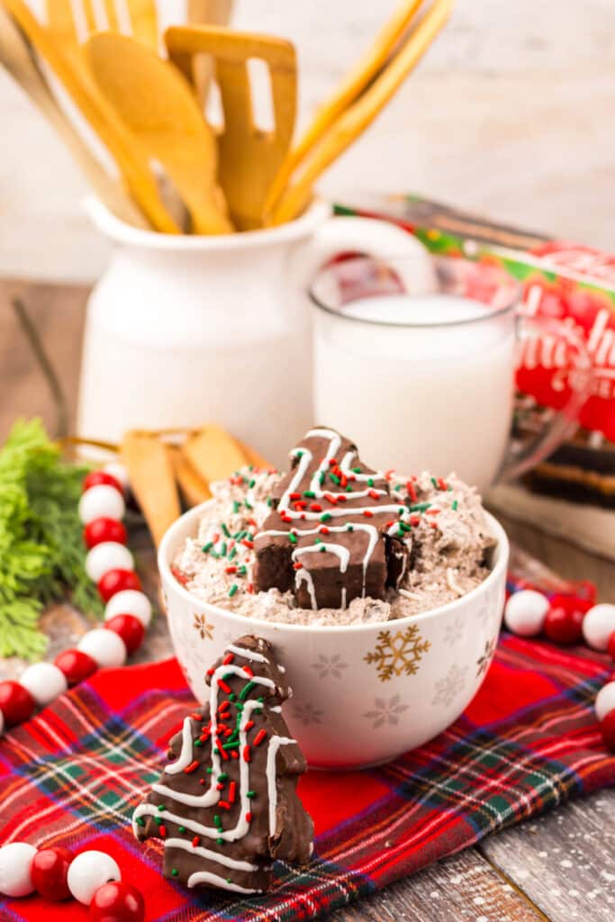 Chocolate Christmas Tree Cake Dip topped with red and green sprinkles and mini Christmas tree cakes on a festive red plaid tablecloth