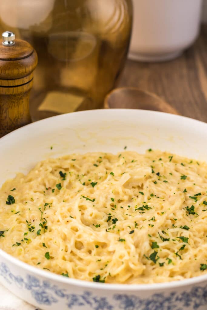 Bowl of creamy garlic parmesan ramen topped with chopped parsley on a white background.
