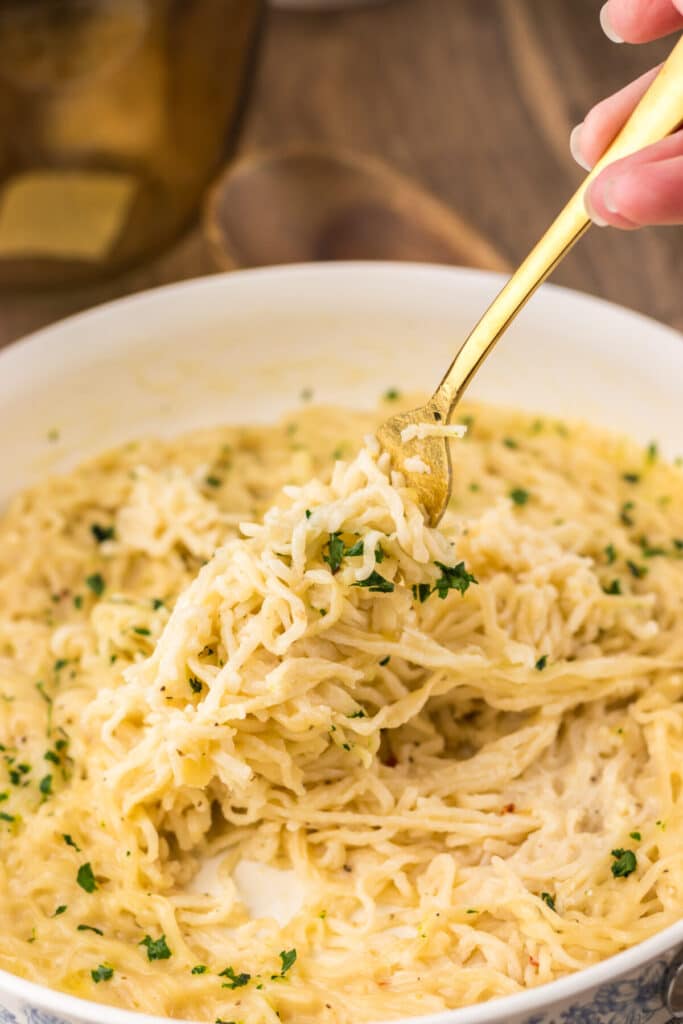 Fork lifting a bite of creamy garlic parmesan ramen from the bowl