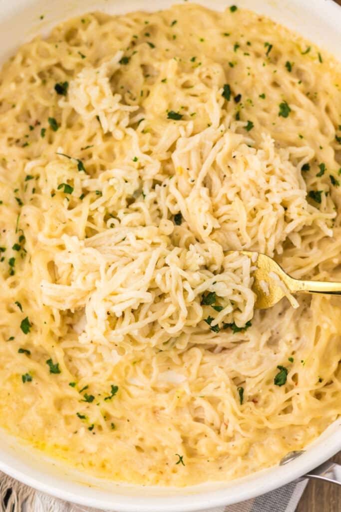 Fork lifting a bite of creamy garlic parmesan ramen from the bowl