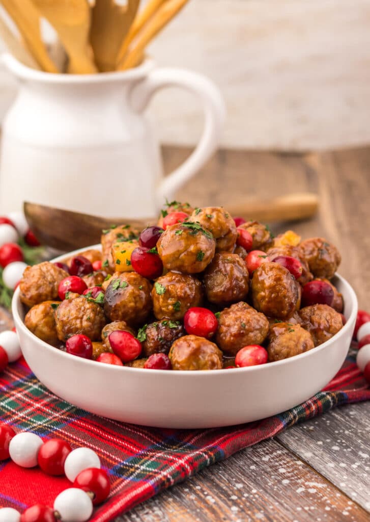 Festive Slow Cooker Cranberry Pineapple Meatballs in a white serving bowl topped with fresh cranberries and parsley