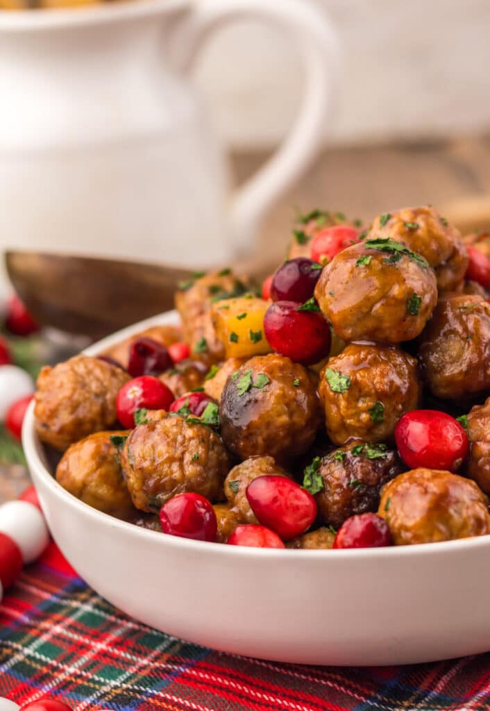 Festive Slow Cooker Cranberry Pineapple Meatballs in a white serving bowl topped with fresh cranberries and parsley