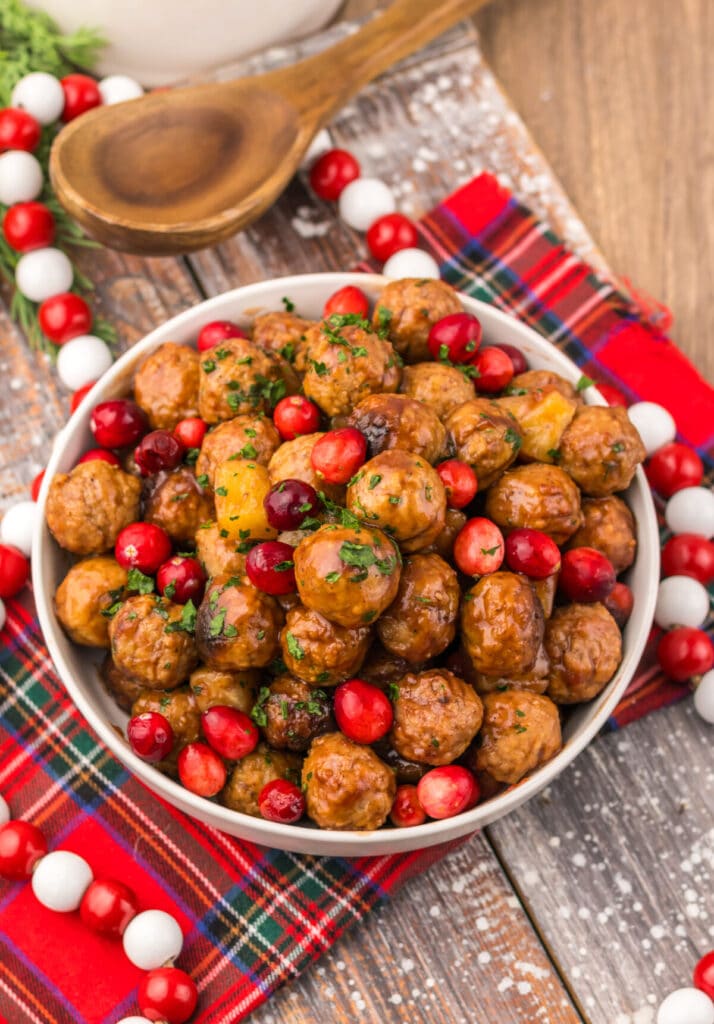 Festive Slow Cooker Cranberry Pineapple Meatballs in a white serving bowl topped with fresh cranberries and parsley