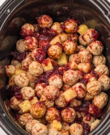 Frozen meatballs in the slow cooker topped with cranberry sauce, pineapple chunks, and BBQ sauce before cooking