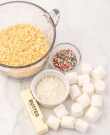 Ingredients for Sugar Cookie Rice Krispie Treats — marshmallows, Rice Krispies cereal, butter, sugar cookie mix, and Christmas sprinkles on a white counter