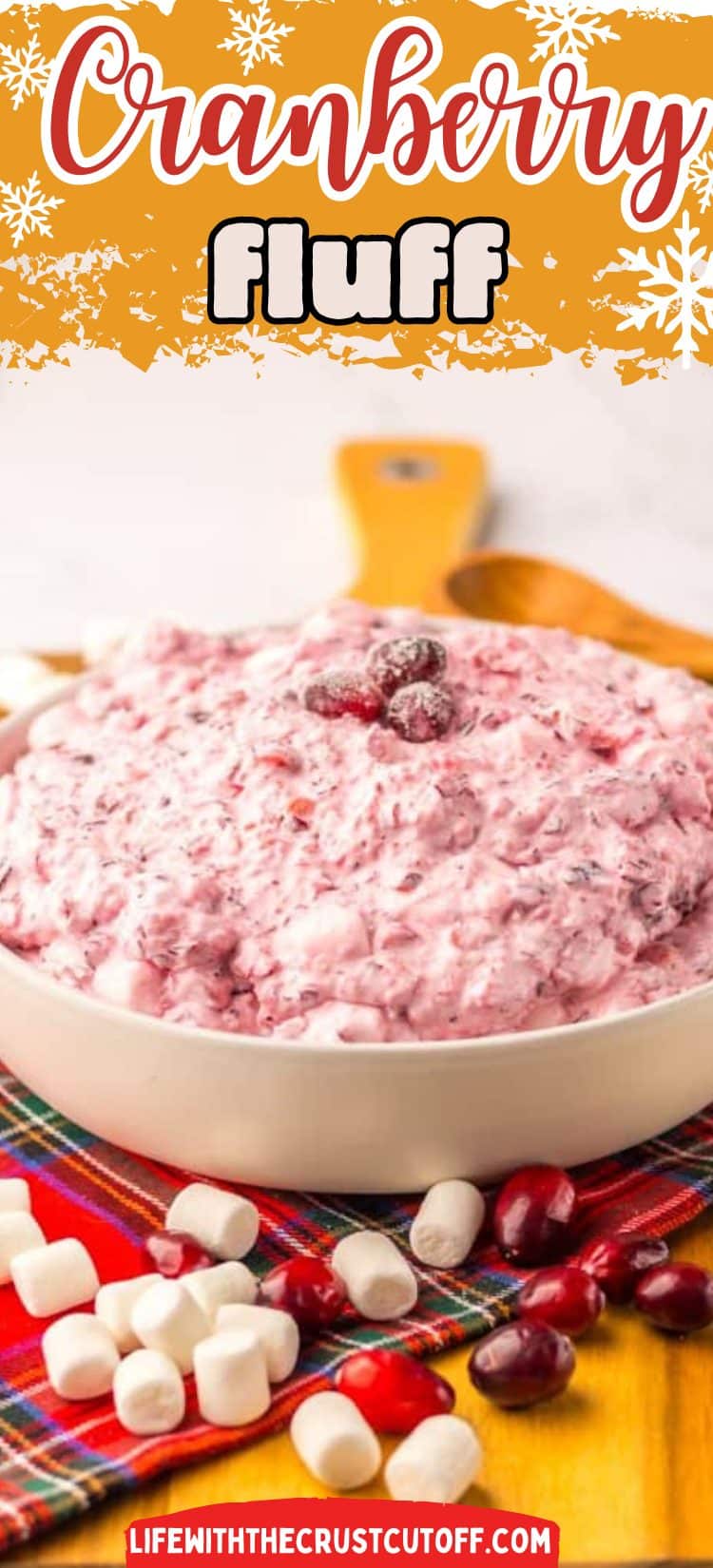 Creamy cranberry fluff dessert in a glass bowl with fresh cranberries on top and holiday decor background