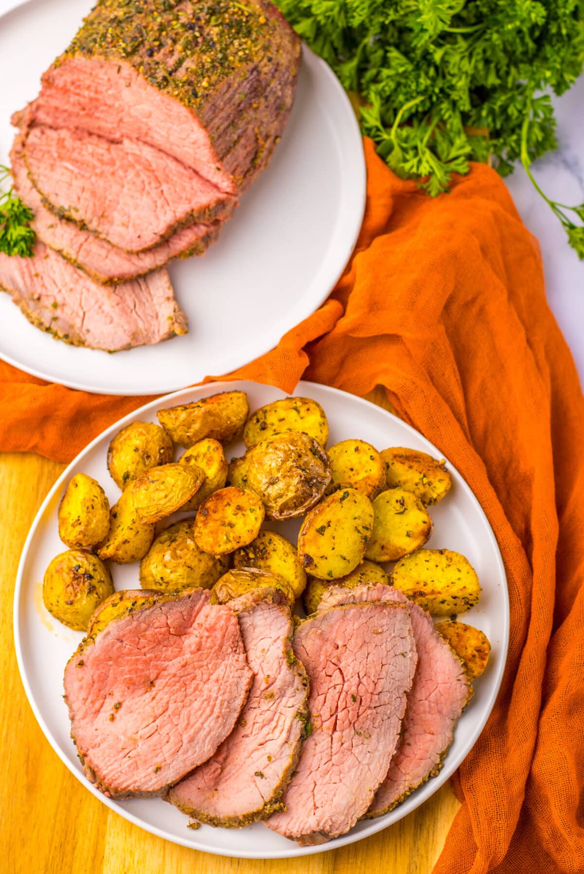 Sliced eye of round roast served with roasted potatoes and pan juices on a dinner plate.
