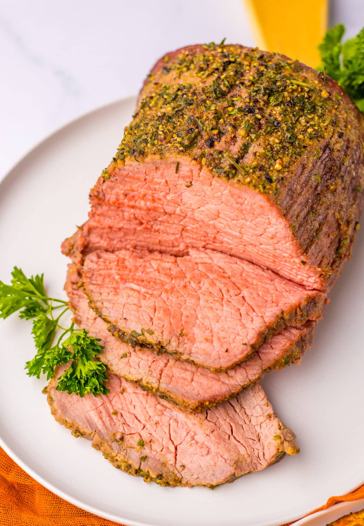 Juicy eye of round roast sliced thin and arranged on a platter with herbs.