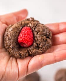 Hand holding a raspberry brownie bomb with a fresh raspberry pressed into the center.