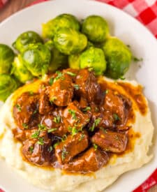 Slow cooker Dr Pepper steak bites served with roasted Brussels sprouts on a dinner plate.