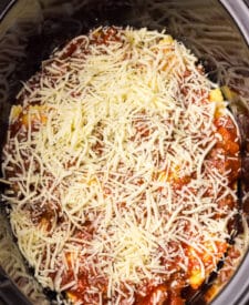 Top view of slow cooker ravioli lasagna covered in shredded cheese