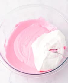 Pink strawberry Cool Whip mixture being stirred in a mixing bowl.