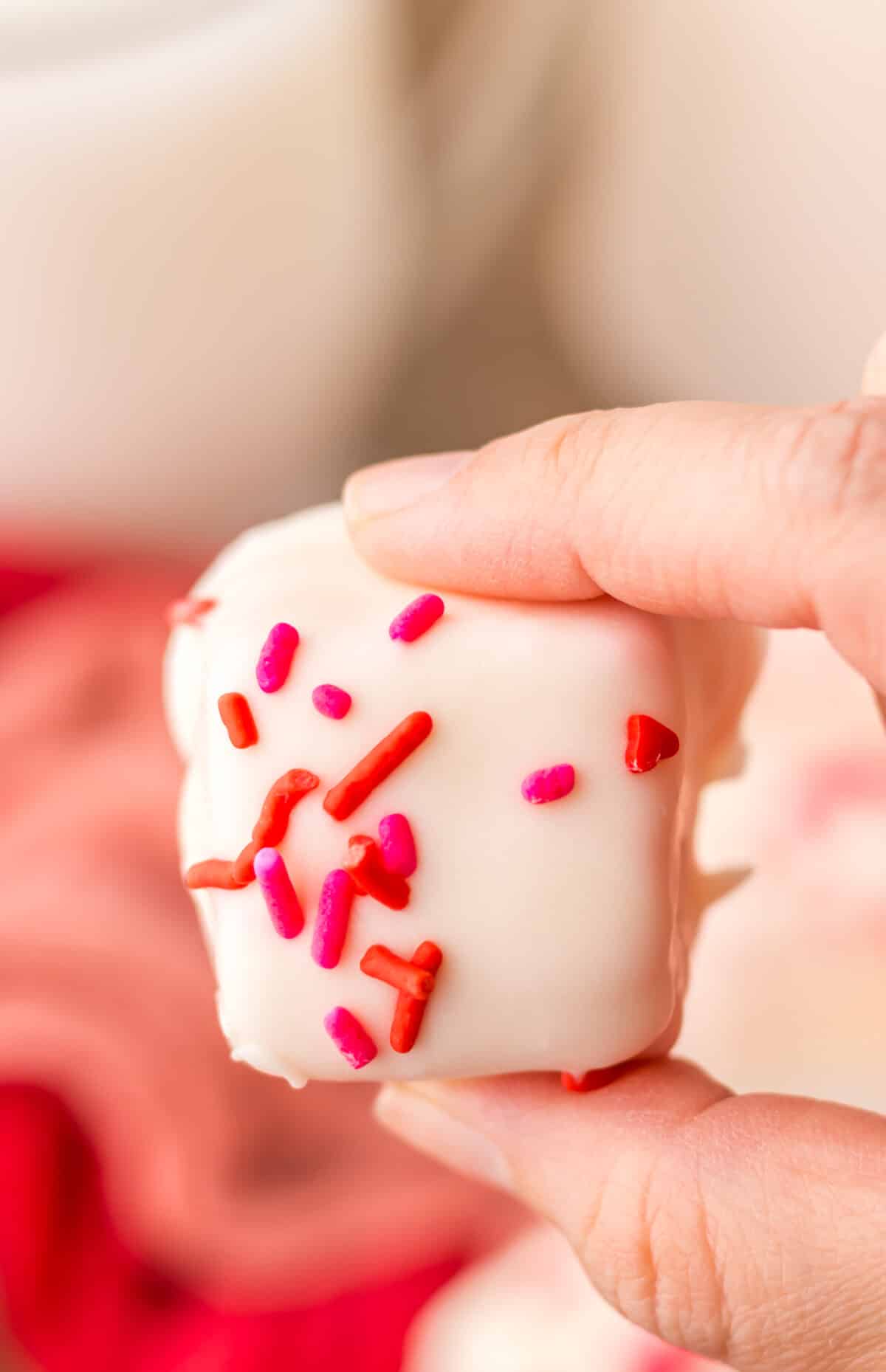 Hand holding a square of strawberry Cool Whip candy showing the creamy pink center.