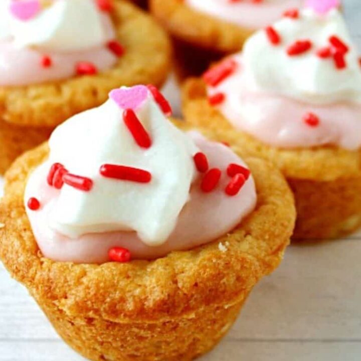 Strawberry cream cheese cookie cups filled with pink creamy frosting and sprinkles on a light surface