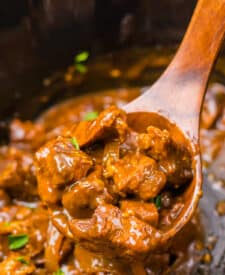 Spoon lifting tender Coca Cola beef tips from the slow cooker.