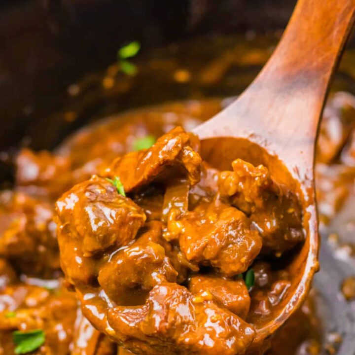 Spoon lifting tender Coca Cola beef tips from the slow cooker.