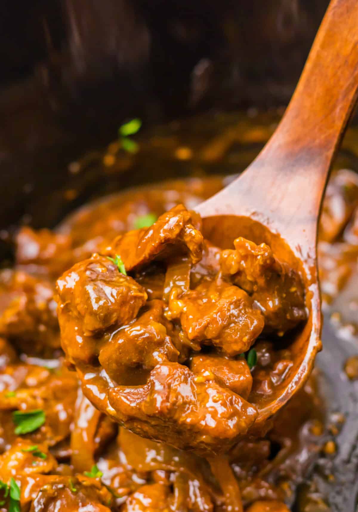 Spoon lifting tender Coca Cola beef tips from the slow cooker.