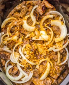 Sliced onions layered over beef tips in the slow cooker.
