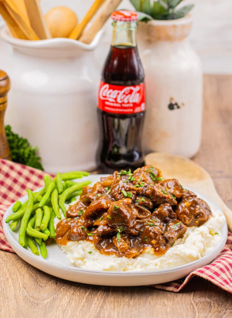 Slow cooker Coca Cola beef tips served over mashed potatoes with green beans on the side.