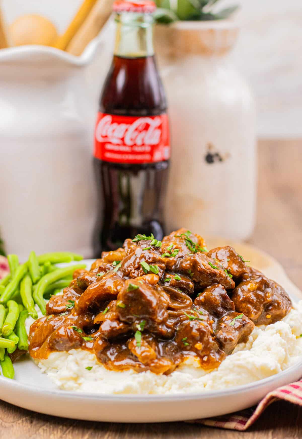 Slow cooker Coca Cola beef tips served over mashed potatoes with green beans on the side.
