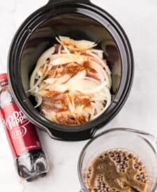 Pork chops placed in the slow cooker with sliced onions and seasonings.