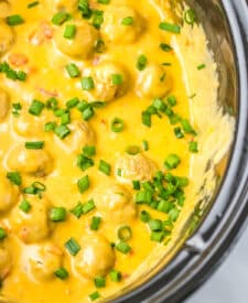 Slow cooker nacho meatballs covered in melted cheese and garnished with green onions.