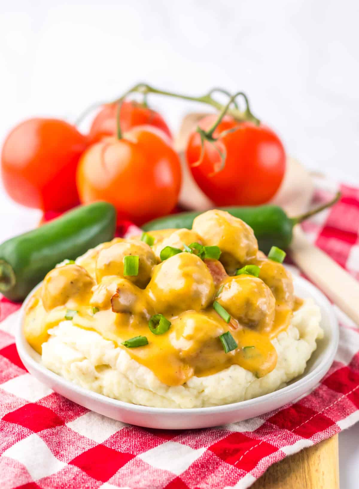 Slow cooker nacho meatballs served over mashed potatoes with tomatoes on the side.