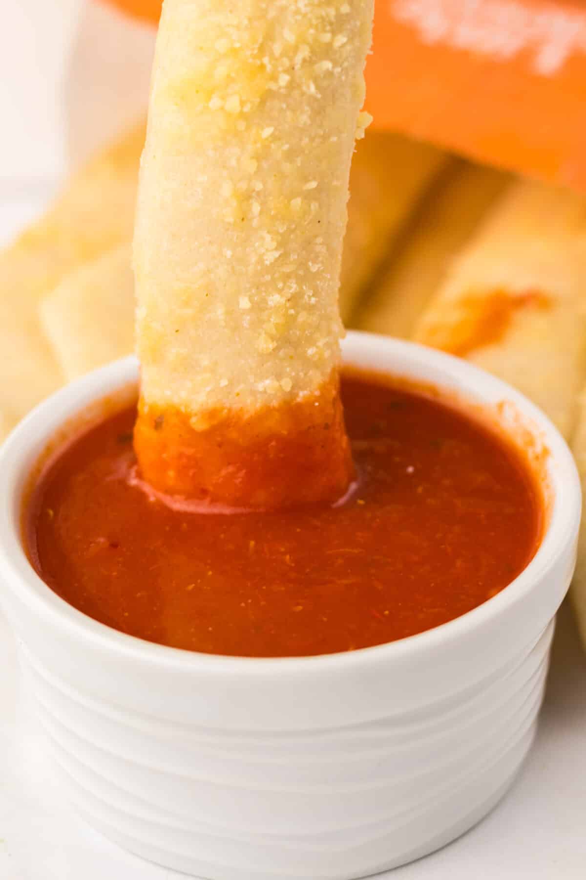 Close-up of crispy homemade Crazy Bread dipped in warm marinara sauce.