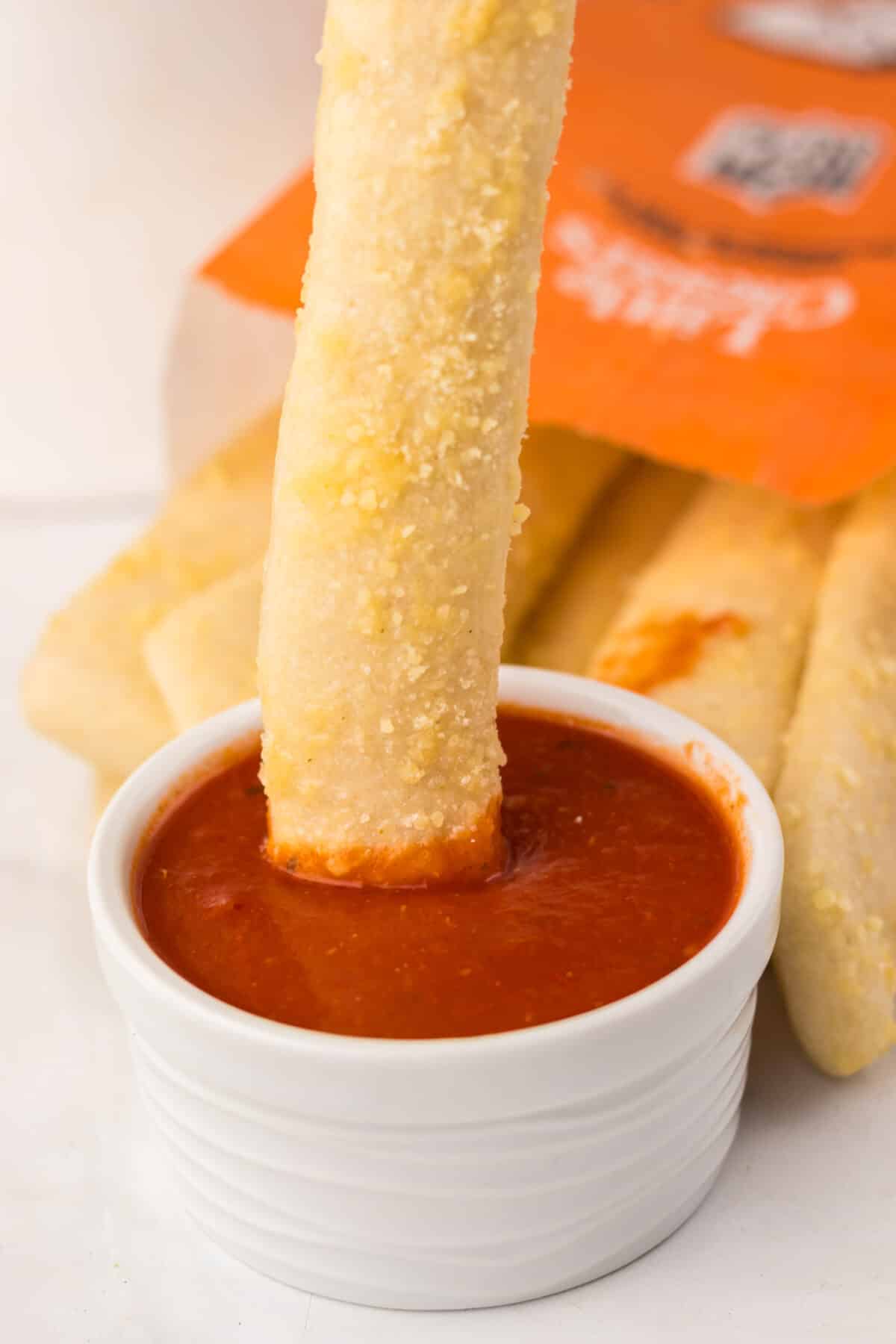 Close-up of crispy homemade Crazy Bread dipped in warm marinara sauce.
