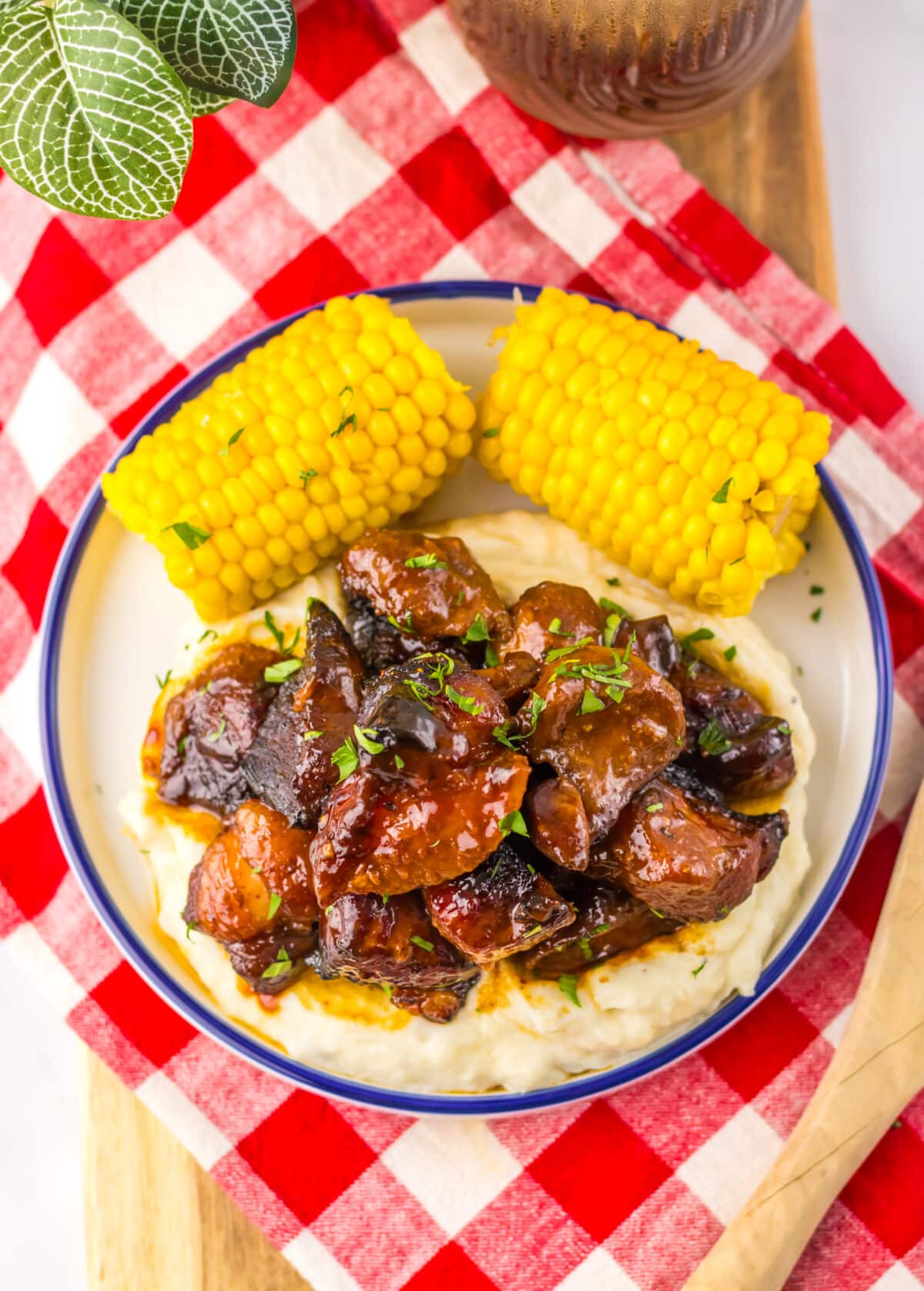 Plate of honey barbecue riblets with corn on a red checkered napkin.