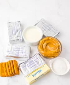 Ingredients for no bake cookie butter cheesecake including cookie butter, cream cheese, and whipped cream.