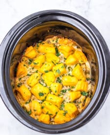 Slow cooker sausage gravy biscuit casserole cooking with melted cheese on top.