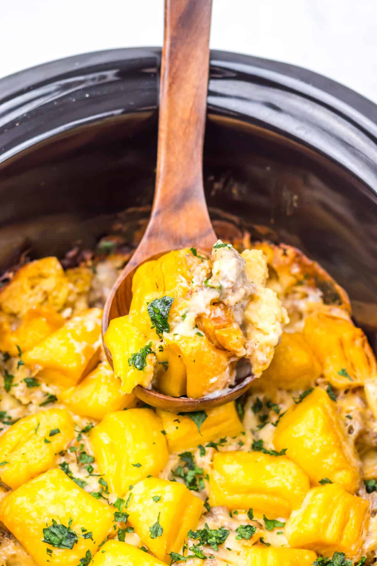 Close-up of slow cooker sausage gravy biscuit casserole being scooped with a spoon.