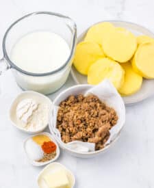 Ingredients for slow cooker sausage gravy biscuit casserole including sausage, biscuits, eggs, cheese, and seasonings.