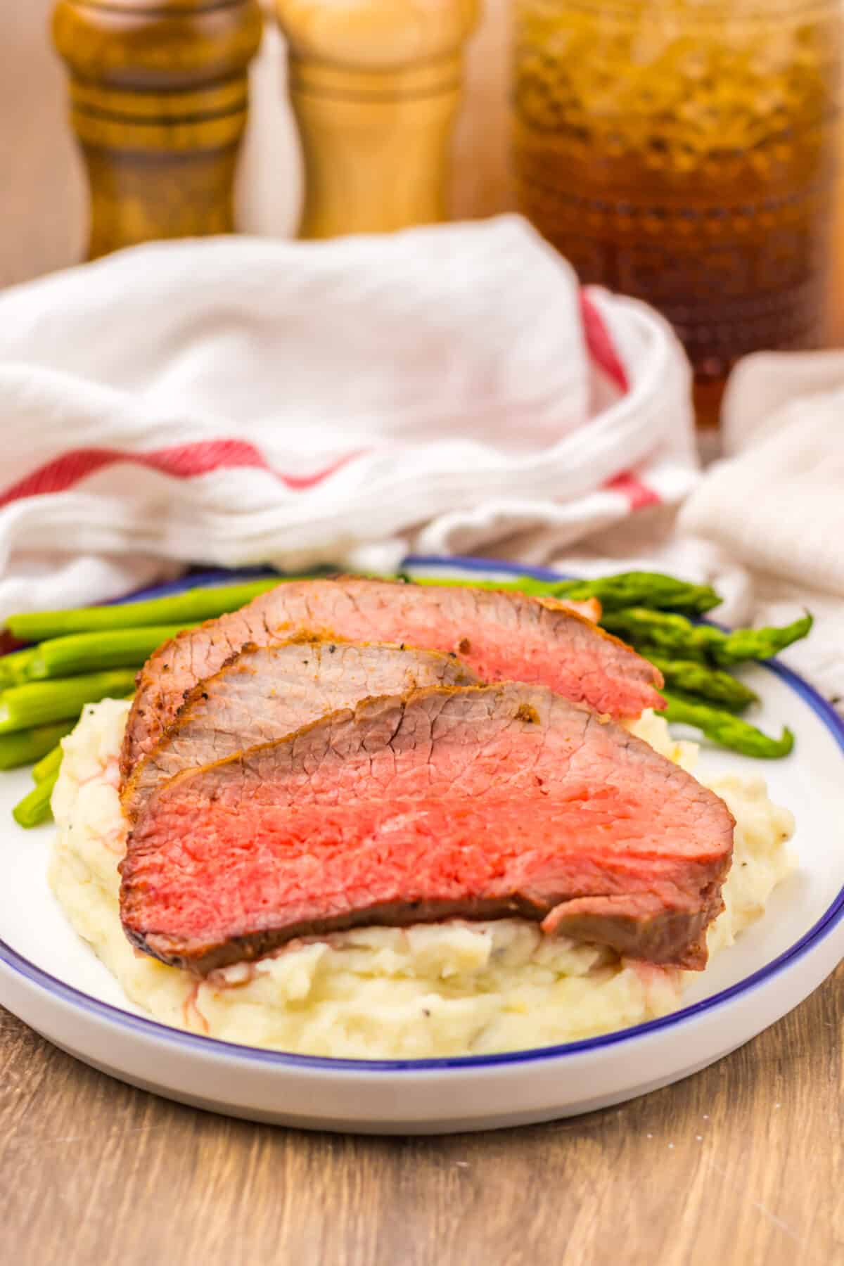 Juicy slices of eye of round roast served over mashed potatoes with asparagus.