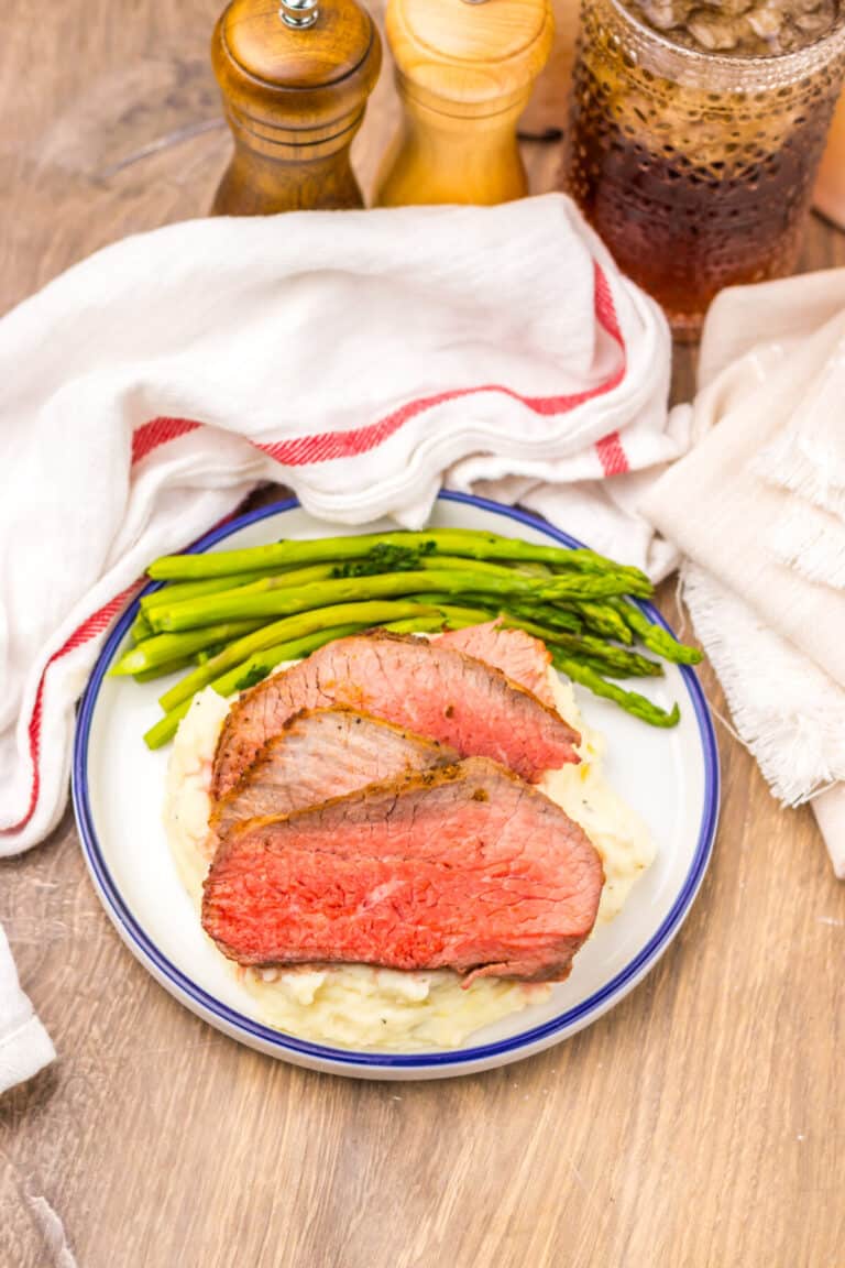 Air fryer eye of round roast served with mashed potatoes and green vegetables.