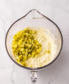 Chopped pickles added to a mixing bowl with dip ingredients.