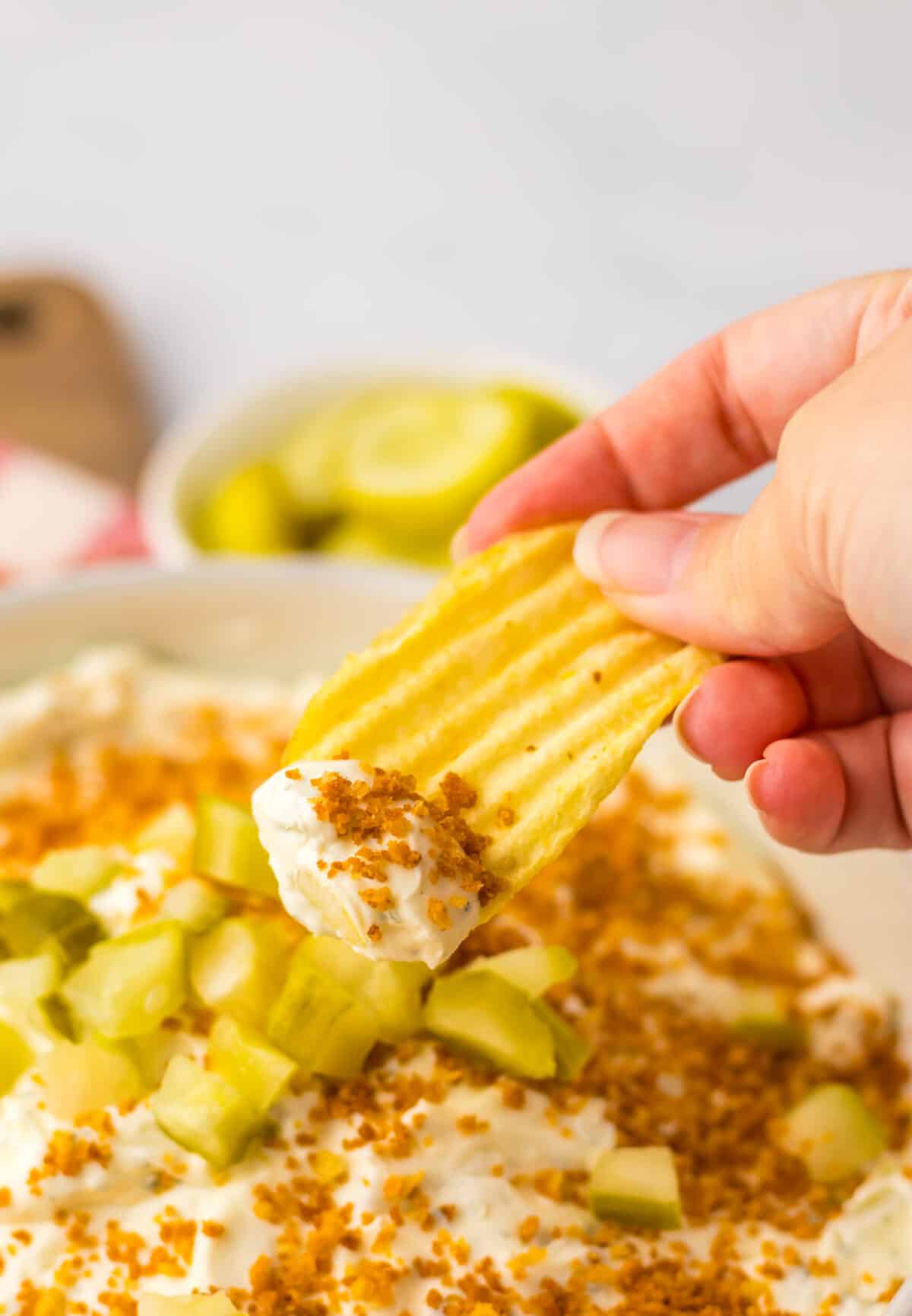 Hand holding a chip scooping creamy fried pickle dip.