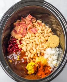 Ingredients being added into a slow cooker for Dr Pepper baked beans.