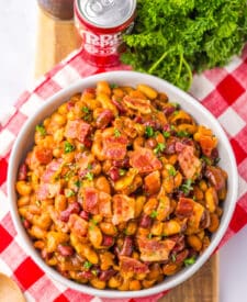 Bowl of baked beans topped with chopped bacon and parsley.