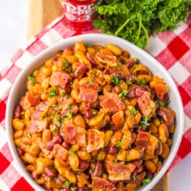 Bowl of baked beans topped with chopped bacon and parsley.