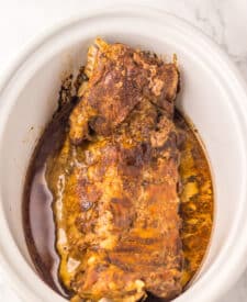 Ribs cooking in sauce in the slow cooker, beginning to tenderize.