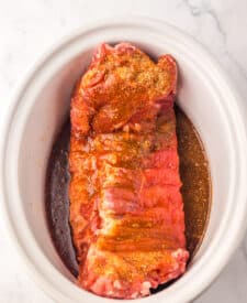 Raw pork ribs coated with seasoning in a slow cooker.