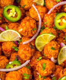 Slow cooker birria meatballs garnished with lime slices, red onion, and jalapeños.