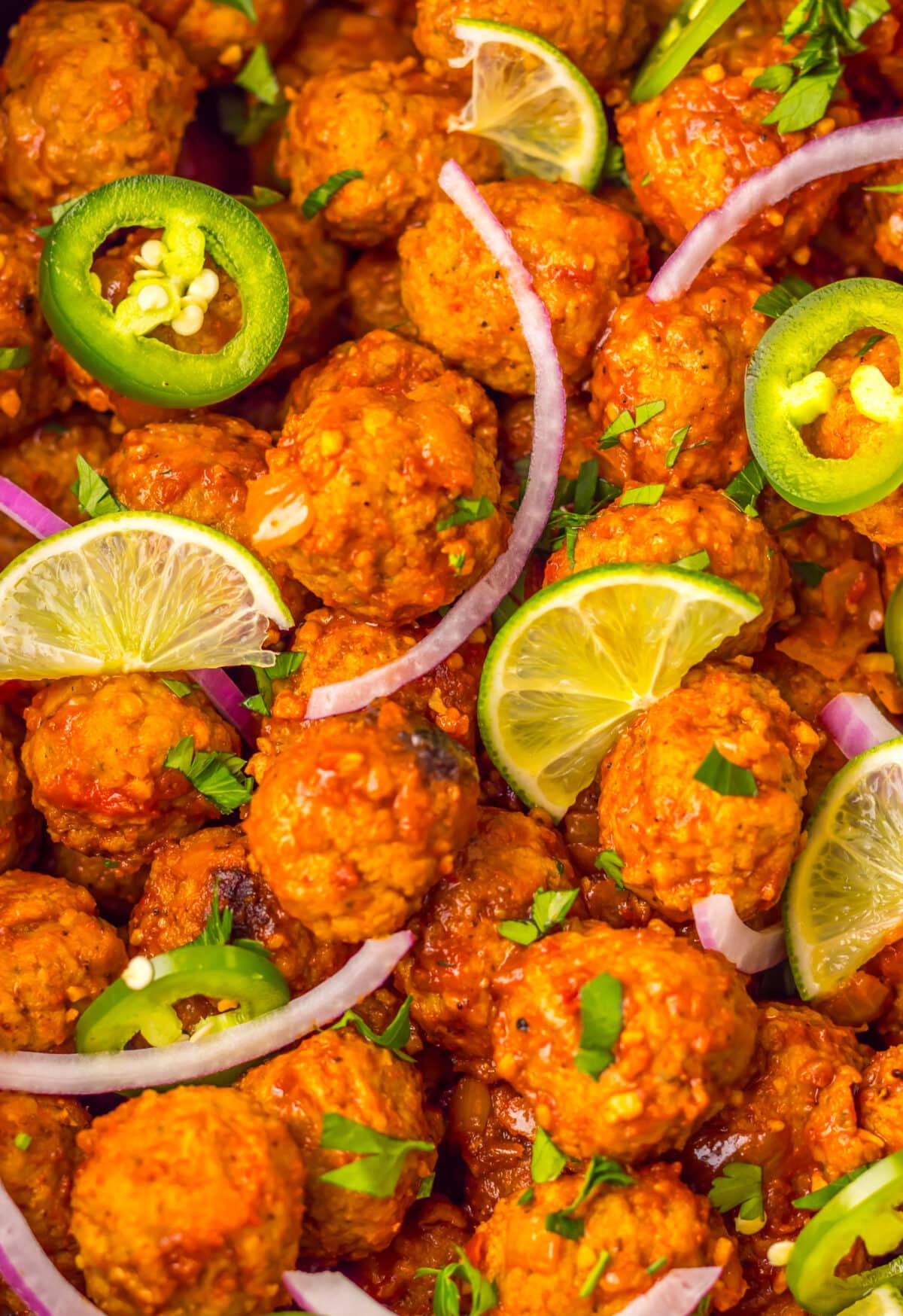 Slow cooker birria meatballs garnished with lime slices, red onion, and jalapeños.