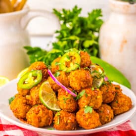 Birria meatballs served on a platter with lime wedges and fresh toppings.